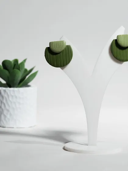 A clean, minimalist shot of modern clay earrings from Dazzle Dangles. The simple prop and white background highlight the product's unique shape and texture.