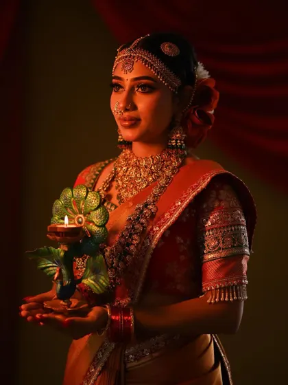 The soft glow of the lamp illuminates the bride's features and the beautiful texture of her red silk saree.