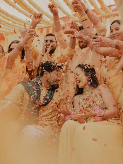 A beautiful candid moment of the couple laughing together as they are showered with petals by their loved ones during the Haldi ceremony.