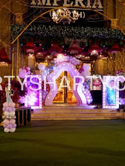 This outdoor princess party entrance uses the venue's greenery as a backdrop, enhanced with a lighted arch, balloon columns, and cutouts of beloved princess characters.