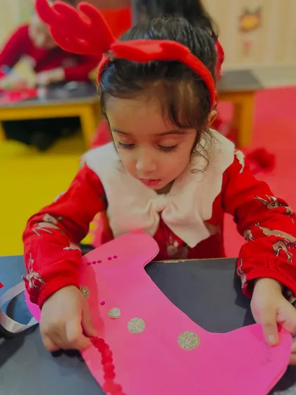 A young girl carefully decorates a pink Christmas stocking, focusing on her creative task.