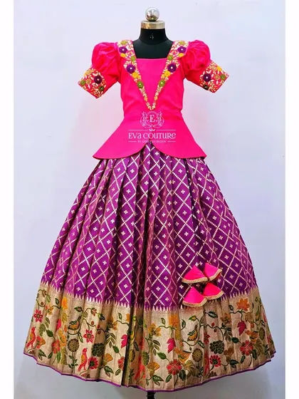 A designer pattu pavadai with a floral border. The magenta peplum top is paired with a purple skirt that has a beautiful woven floral design along the hem.