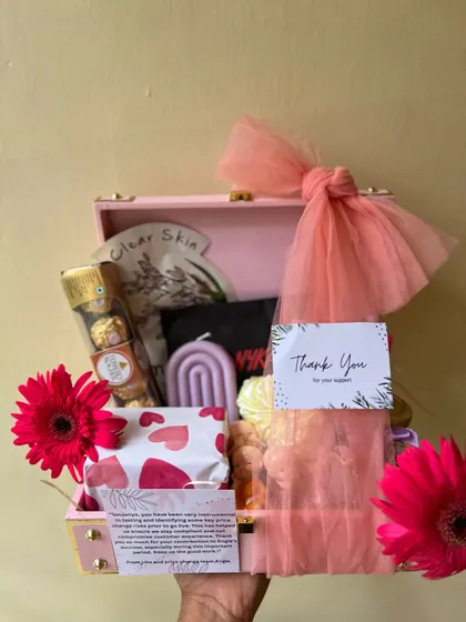 Holding up the 'Thank You' hamper to show its size and the beautiful arrangement of gifts inside the pink suitcase box.