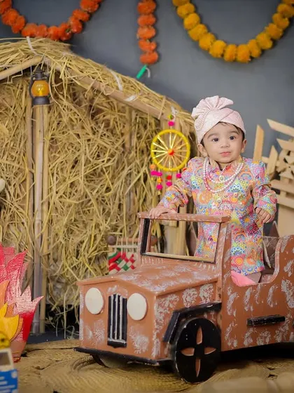 This little sardar is celebrating his first Lohri in style, sitting in a mini jeep with a bonfire prop and festive decorations all around.