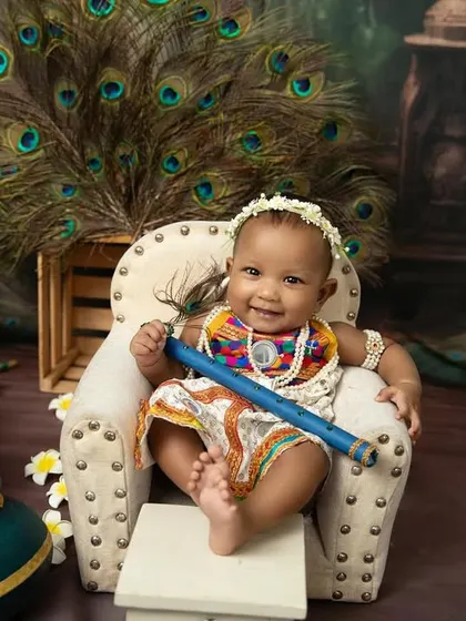 A happy baby Krishna holding his flute, ready to charm everyone. The peacock feather backdrop adds a touch of divine beauty.