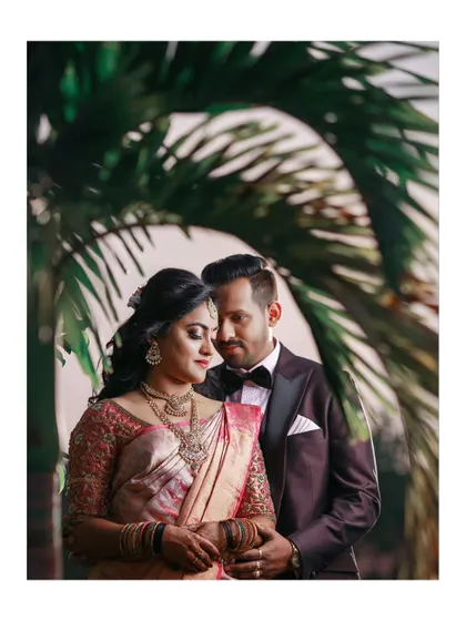 A romantic portrait of the couple, the groom embracing the bride, framed by lush palm leaves.