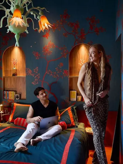 The 'Folly' design from Fromental in the 'Wilde Dreams' colorway. This bedroom scene showcases the delicately embroidered swallows and bees on a deep teal background, creating a romantic and symbolic narrative.