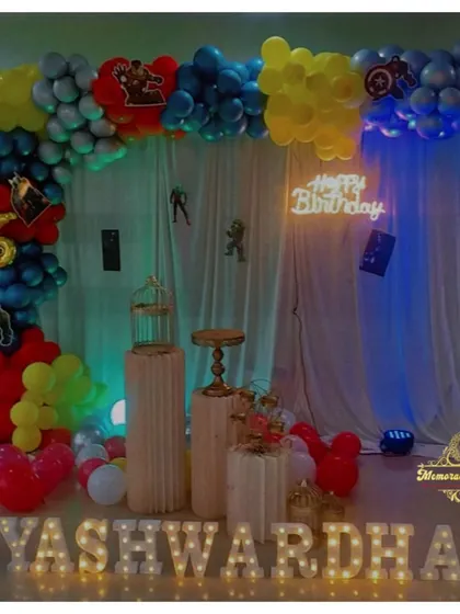 An Avengers-themed birthday party setup with a colorful balloon arch and character silhouettes against a sheer curtain backdrop.