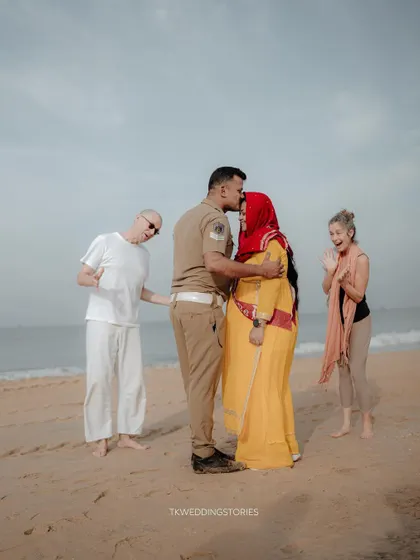 A candid and heartwarming moment from a beach maternity shoot, where a couple shares a kiss while strangers in the background cheer them on.
