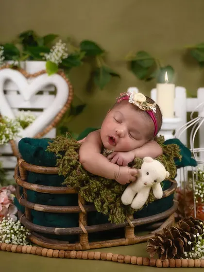 This cozy, rustic setup features a baby sleeping in a wooden sleigh, surrounded by pinecones, greenery, and a warm, mossy blanket.