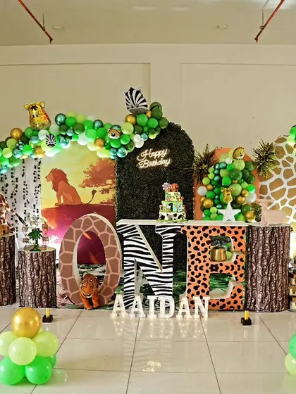 A magnificent jungle-themed first birthday party. This large-scale setup includes a giraffe cutout, animal-print "ONE" letters, and a lush green balloon arch, creating an impressive safari scene.