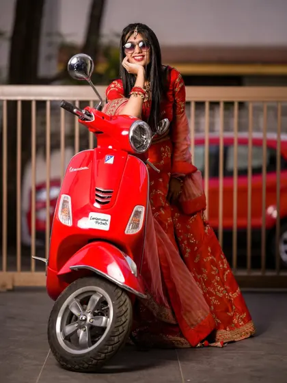 The full look of the modern Vespa bride, showing off her red lehenga and cool sunglasses against an urban backdrop.