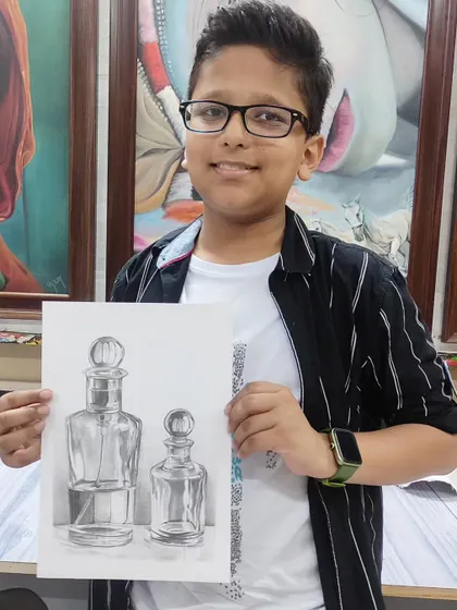 A young student proudly holding his impressive still life pencil drawing of glass bottles. We teach students of all ages how to observe and render objects with accuracy and detail.