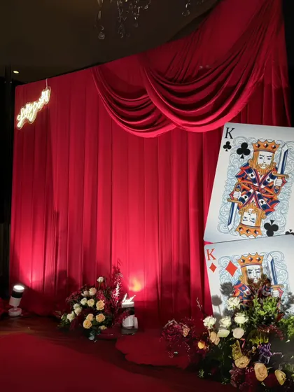 Another angle of the giant playing card props and rich floral decor, highlighting the dramatic uplighting that enhances the theatrical feel of the stage.
