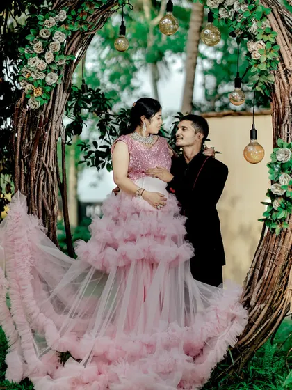 A romantic maternity couple portrait in a beautiful outdoor setting. The expecting mother is wearing a pink sequin and ruffle gown, one of many options available for rent.