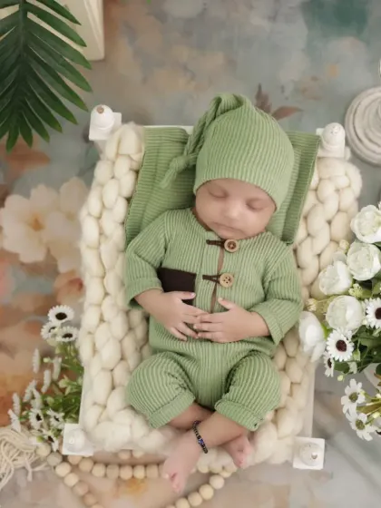 An overhead view of the newborn in a green outfit. The floral background and soft lighting create a dreamy and artistic composition for this baby boy's photoshoot.