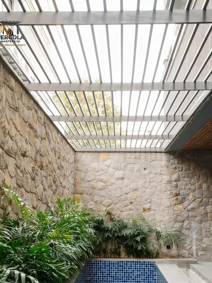 This rafter pergola is built within a courtyard, framed by stone walls and overlooking a small pool. The design creates a private, tranquil retreat that feels both rustic and modern.
