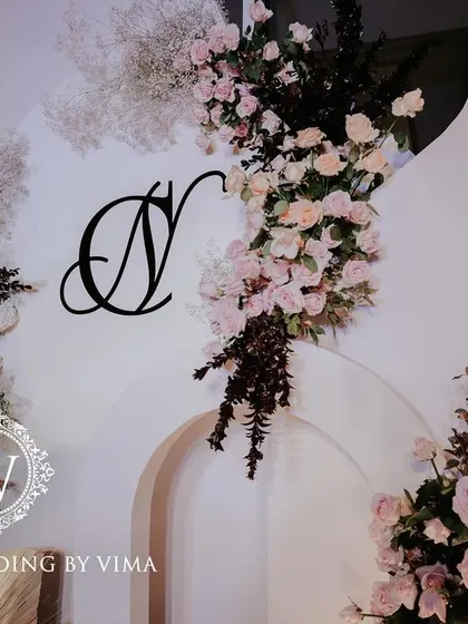 A classic and elegant reception setup symbolizing everlasting love. The stage features a modern, minimalist backdrop with custom monograms, floral arrangements, and soft lighting.