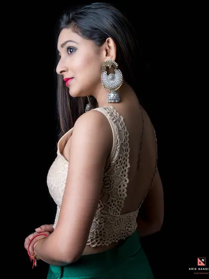 A profile shot highlighting the model's back and a large statement earring. The low-key lighting creates a dramatic effect, emphasizing her glowing skin and the details of her lace top.