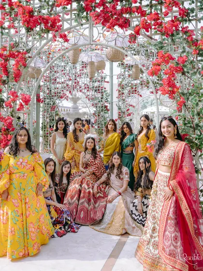 A beautiful group portrait of the bride with her bridesmaids, all dressed in vibrant colors under a floral arch.