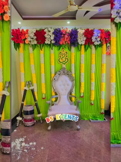 This traditional stage decoration uses vibrant lime green drapes with colorful floral arrangements. The ornate silver chair and traditional instruments on the side complete the setup for a puberty ceremony or other family function.