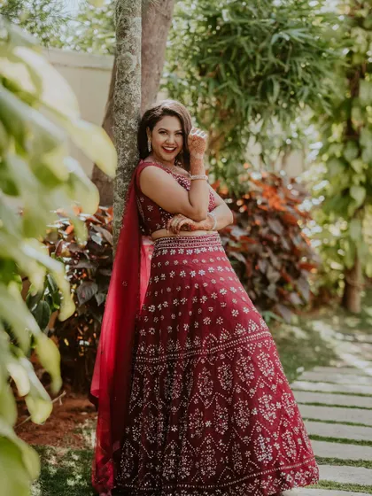 A joyful, candid shot in a garden setting. The bride's red lehenga and happy smile are the focus of this beautiful image.