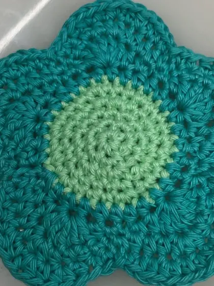 A close-up of one of the flower coasters, showing the two-tone color design and neat spiral stitching in the center.