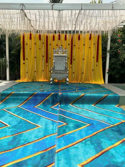 This wide shot shows the complete outdoor stage with its unique blue and gold patterned carpet leading up to the throne. This kind of setup is great for making a bold statement at a sangeet or reception.