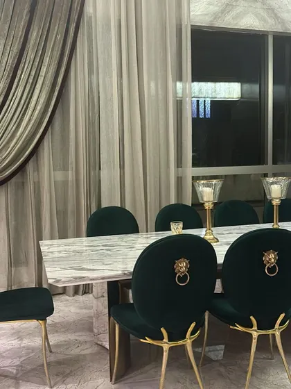 A perfect dining scene featuring our emerald green velvet chairs with their signature lion head knockers and sculptural gold legs.
