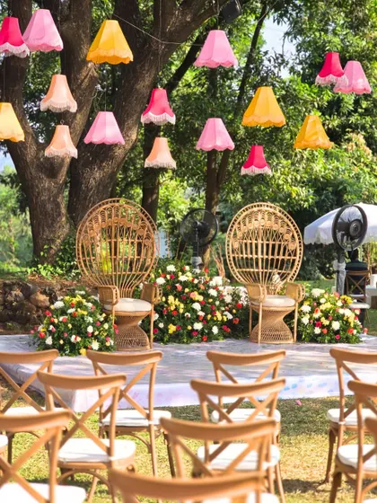 The main seating area for the 'Artistic Atelier' Haldi, featuring peacock chairs, colorful hanging lampshades, and a backdrop of flowers.
