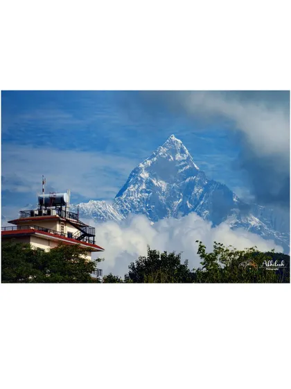 A classic view of Machapuchare peak rising above the clouds, with a local teahouse in the foreground, blending culture and nature.
