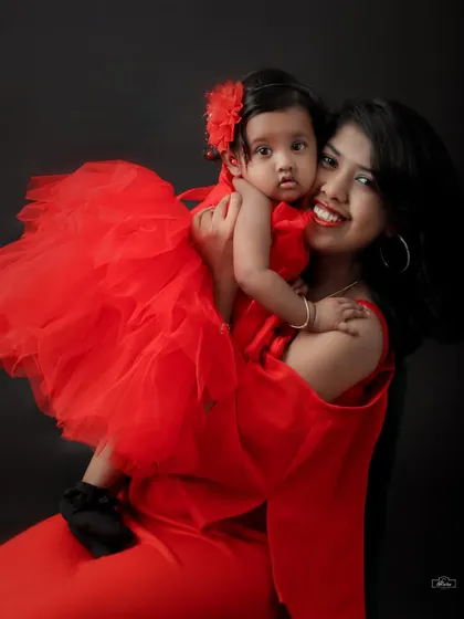 A beautiful high angle shot of a mother holding her daughter, both radiant in red. This studio portrait captures a loving and joyful moment between them.