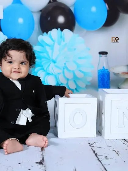 A baby boy in a black suit leans against "ONE" blocks in this stylish Boss Baby shoot. His serious expression adds to the humorous and charming theme.