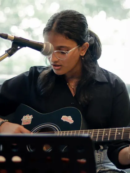 A student singing and playing guitar, showcasing her singer-songwriter talents at a recital.