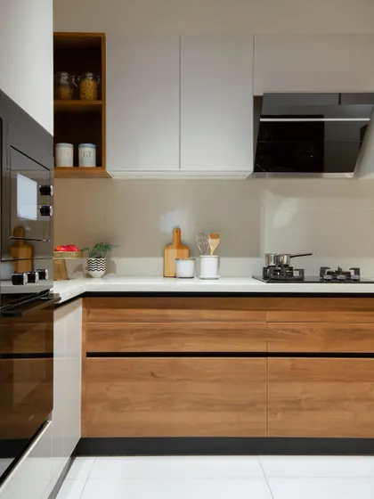A clean and efficient kitchen layout. We paired handleless wood-finish lower cabinets with matte white upper cabinets for a balanced, two-tone look. The design includes a built-in oven and a sleek black chimney hood, ensuring the space is as functional as it is stylish.