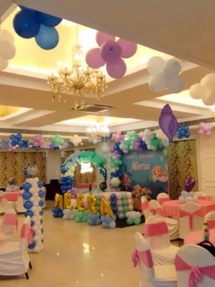 A wide view of a hall decorated for a kids' theme party, showing multiple elements like ceiling decor, balloon pillars, and a stage backdrop working together.