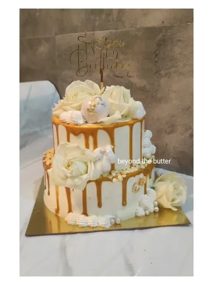A full view of this elegant two-tier white and gold drip cake, adorned with beautiful white roses. It's a versatile design that works wonderfully for birthdays, anniversaries, or even small weddings.