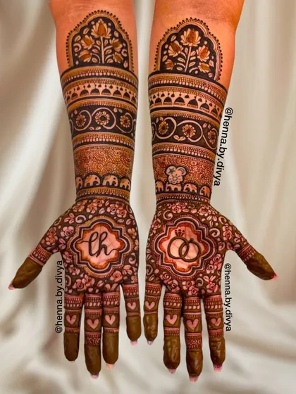 A beautiful example of a full-hand engagement mehendi. This design features the couple's initials 'LH' and a symbol of two rings, surrounded by intricate floral and elephant motifs.