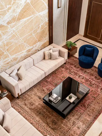 This top-down view shows how different elements come together to form a cohesive living area. The rich, patterned rug anchors the space, while the neutral sofas are accented with pops of deep blue. The marble feature wall adds a touch of luxury and texture.