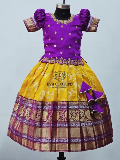 A similar design in yellow and purple, this pattu pavadai features a pleated yellow skirt and a purple blouse with puff sleeves and delicate embroidery.
