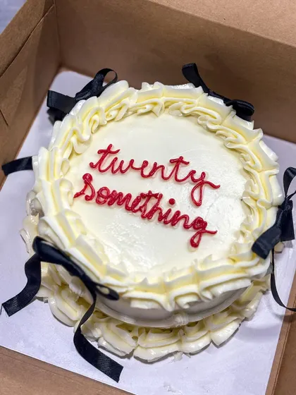 This "twenty something" bento cake is a perfect example of the trendy vintage buttercream style. It features elegant off-white piping and delicate black ribbon bows for a chic and celebratory look.