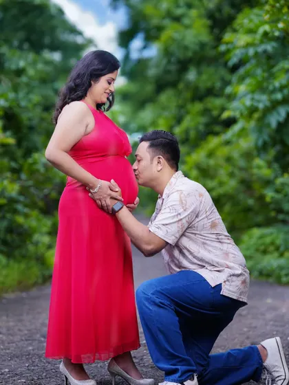 A classic pose where the partner kneels to kiss the baby bump. Captured on a path surrounded by lush greenery, this image feels intimate and connected to nature.