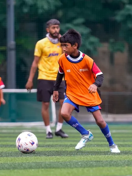 A player in an orange bib looks for a passing option. Our drills emphasize teamwork and intelligent movement off the ball.