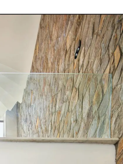 A detail shot where the glass balustrade meets the textured stone wall, highlighting the contrast of modern and rustic materials.