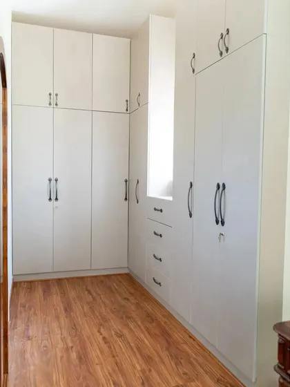 A spacious walk-in closet with ample storage, featuring clean white cabinetry and classic black handles. The design maximizes space while maintaining a bright and organized feel.