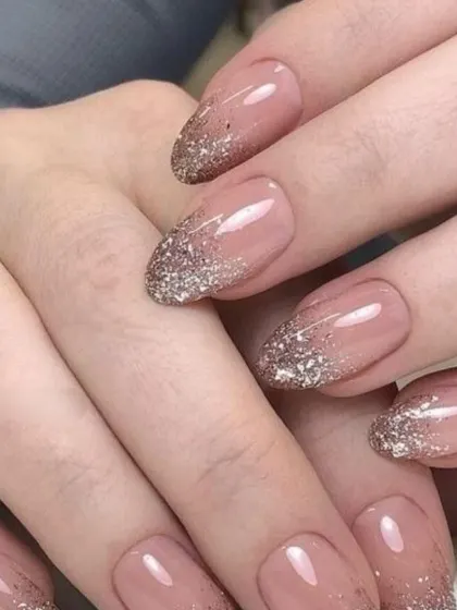 A beautiful glitter gradient effect on long, oval-shaped nails. The silver glitter cascades down from the tip over a sheer nude base, creating a dreamy and ethereal effect that's perfect for a romantic bridal look.