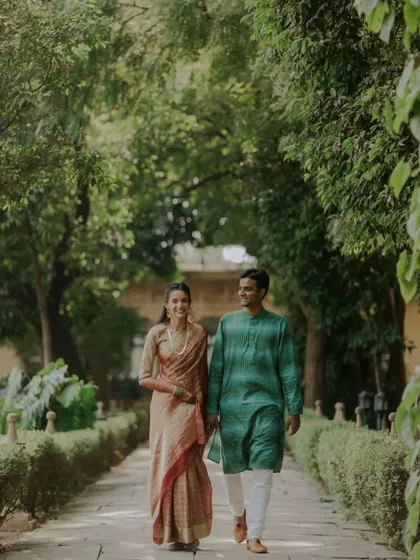 A beautiful shot of a couple in traditional South Indian attire, taking a peaceful walk through a lush green pathway.