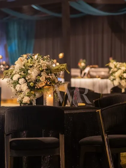 A simple yet elegant table setting for a sangeet night. A bouquet of white roses and baby's breath sits on a black sequined tablecloth, creating a classic and sophisticated look.