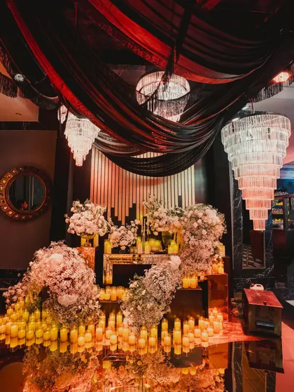 A stunning decor installation featuring cascading white florals, hundreds of candles, and dramatic black and red ceiling drapes.