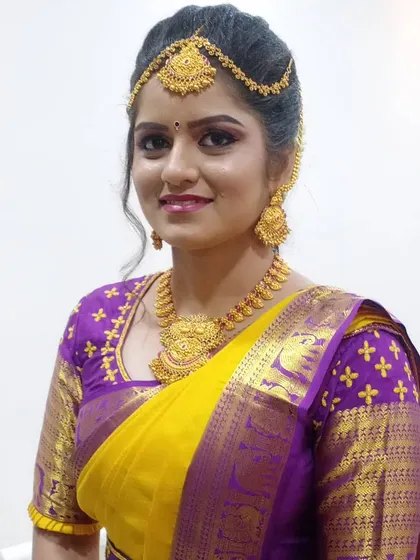 A close-up of another beautiful bride in a yellow and purple Kanjeevaram saree. Her makeup features a soft pink lip and defined eyes, paired with a traditional three-layered matha patti.